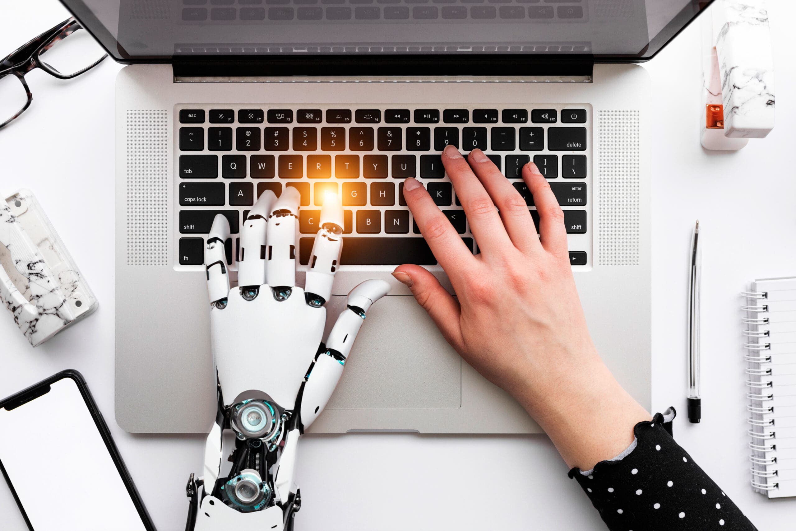 Image showing a human and a robot hand over a laptop symbolizing the theme of the blog post which is harmonizing human writing and ai
